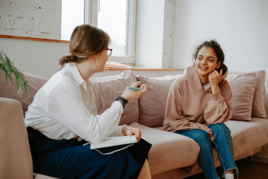 A wellness coach and young client engaging in a warm counseling session on a cozy sofa.